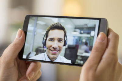 Hands holing mobile phone with video of a man with a headset