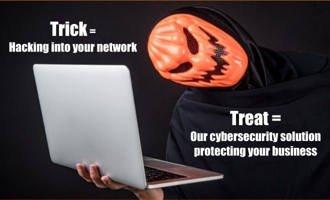 Hooded figure in an orange jack-o-lantern mask holding a laptop: the trick is hacking into your network, the treat is our cybersecurity solution protecting your business.