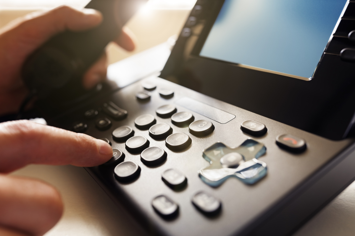 Close up of a phone, with the receiver being lifted and a finger outstretched to dial a number.