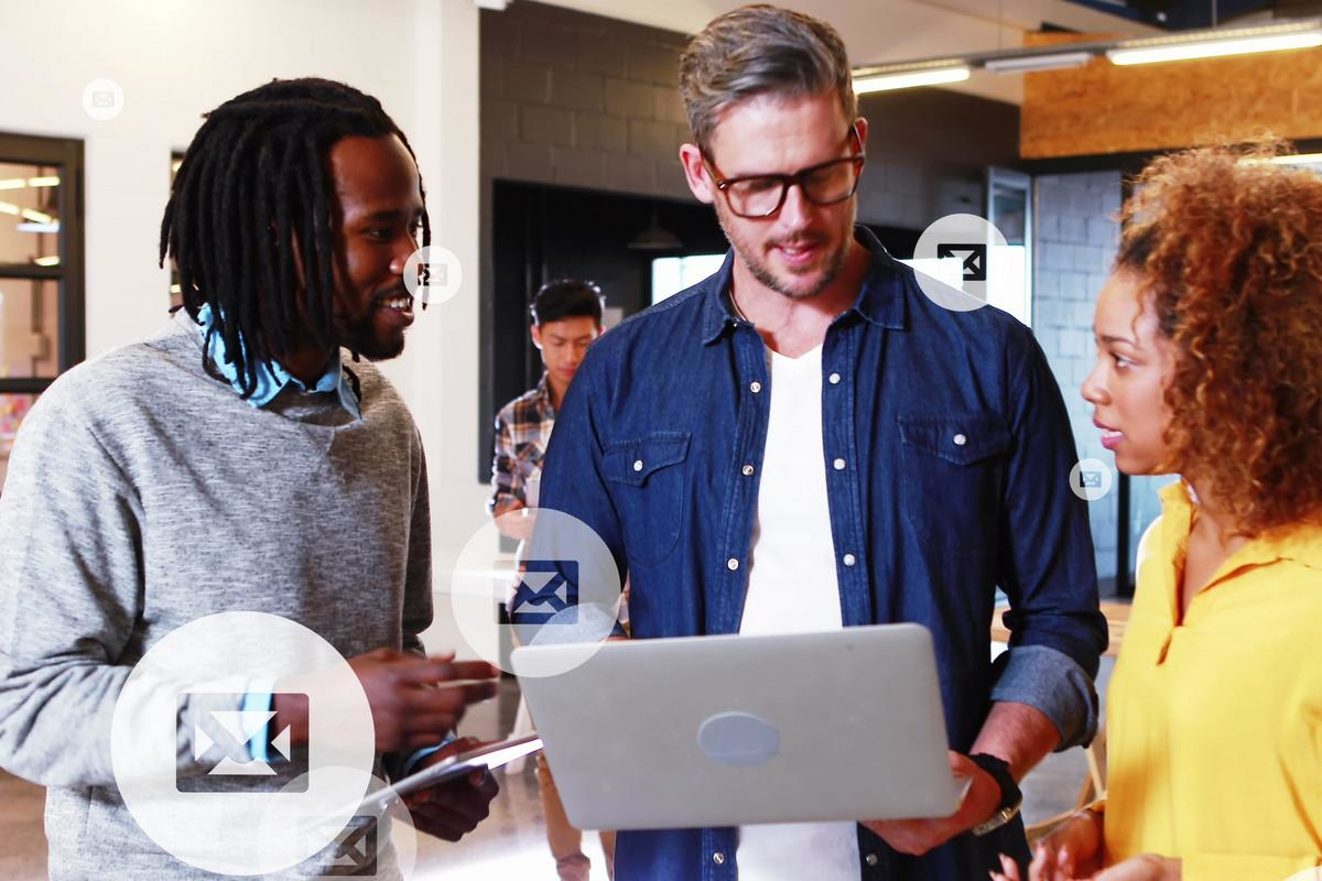 Three coworkers reviewing email together on a laptop in a modern office.