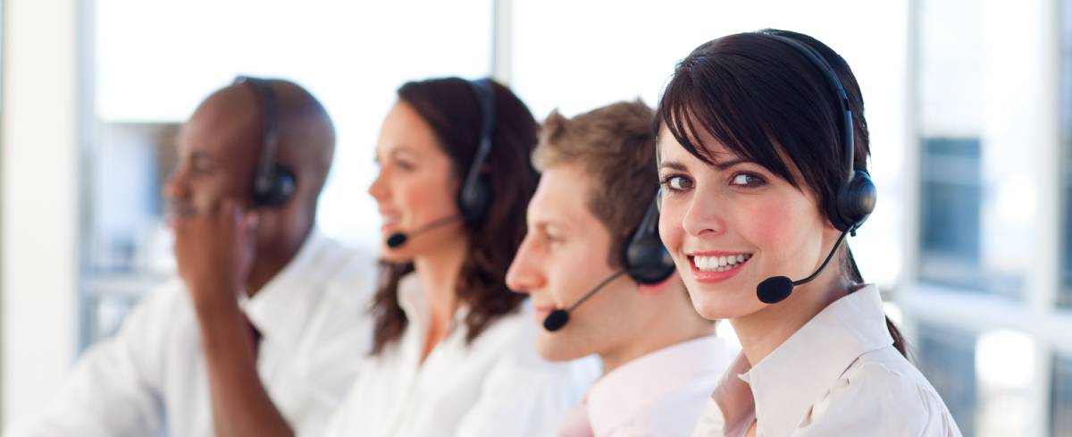 A help desk employee smiling at the camera with 3 more employees in the background