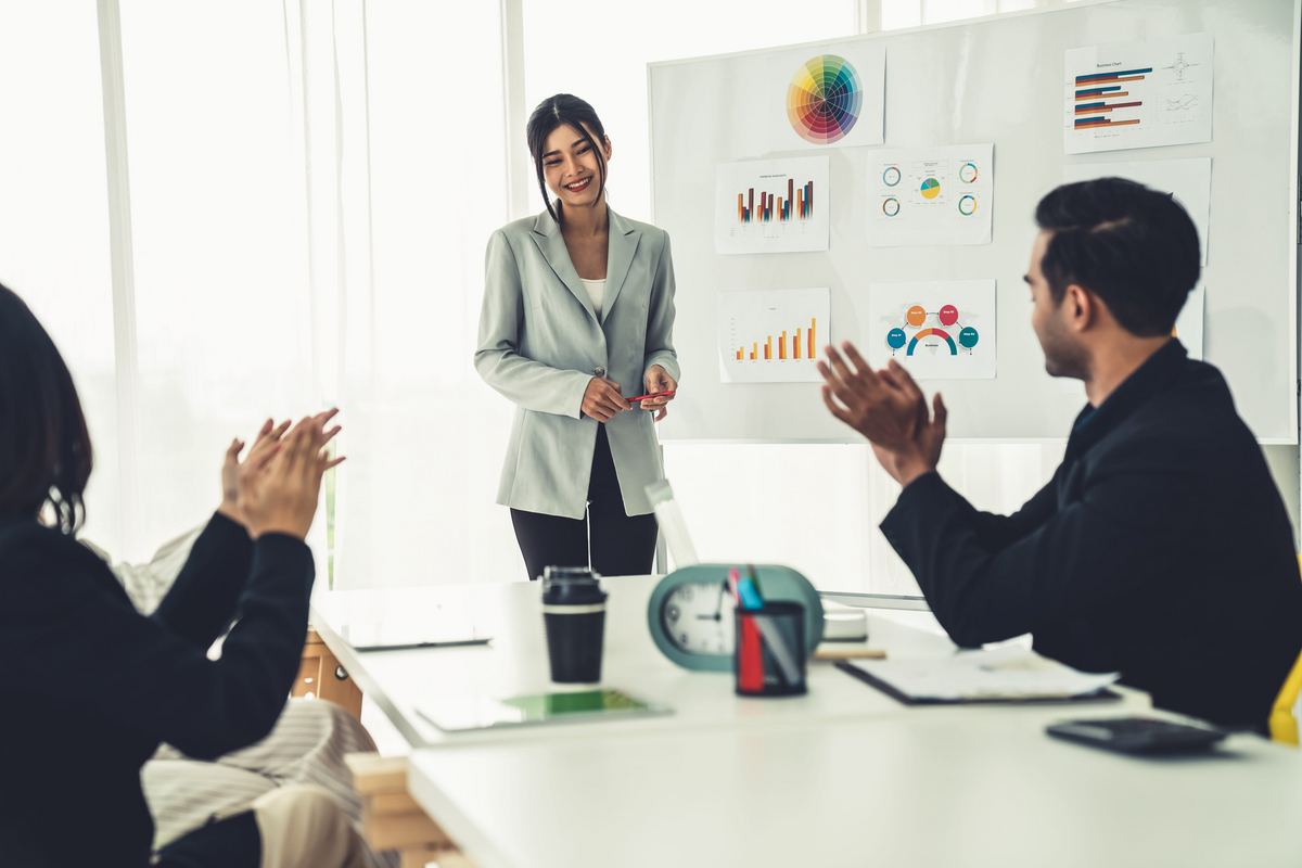 Team member presenting growth charts on a whiteboard while seated colleagues applaud during a planning meeting.