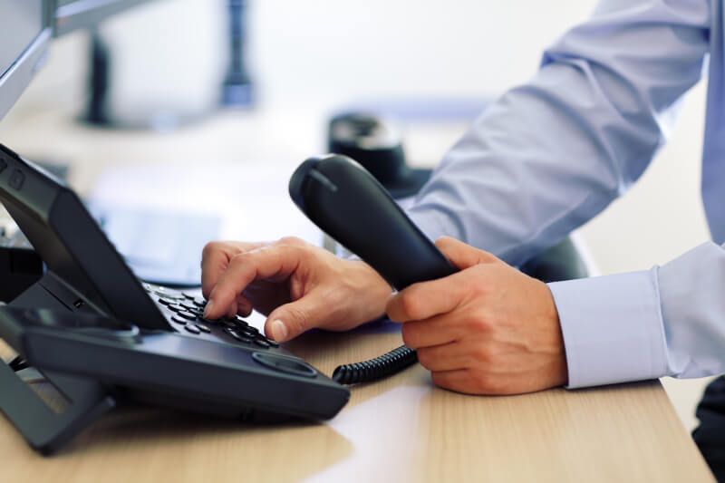 Businessman holding a desktop IP phone handset and dialing a number