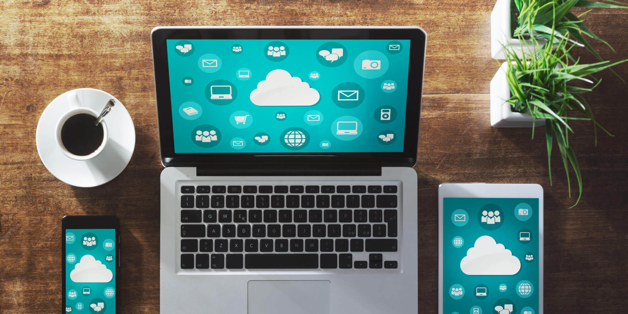 Laptop, phone, and tablet sitting on a wooden desk and displaying the same green screen filled with cloud icons