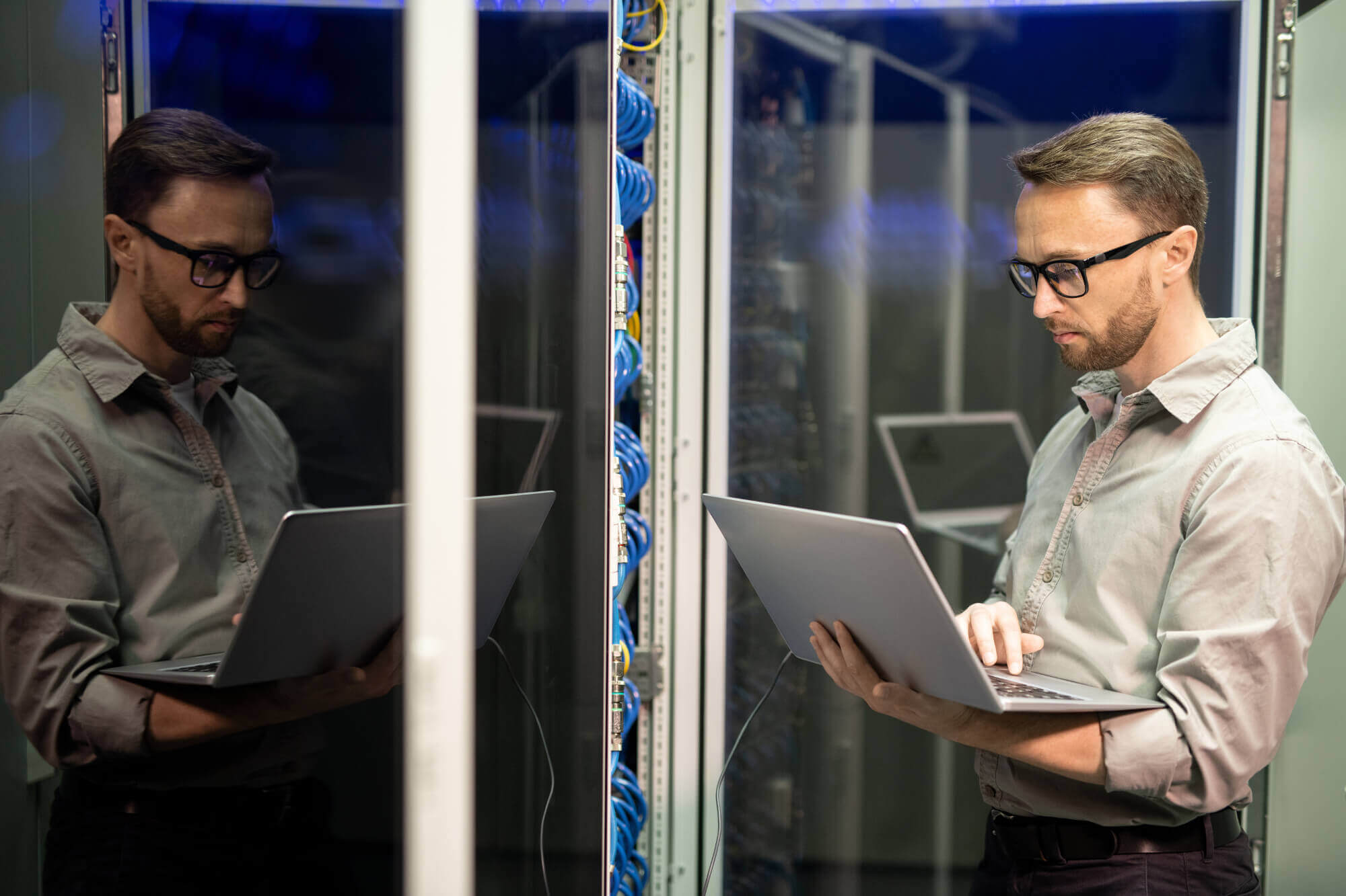 Data technician wearing glasses using a laptop in a server room