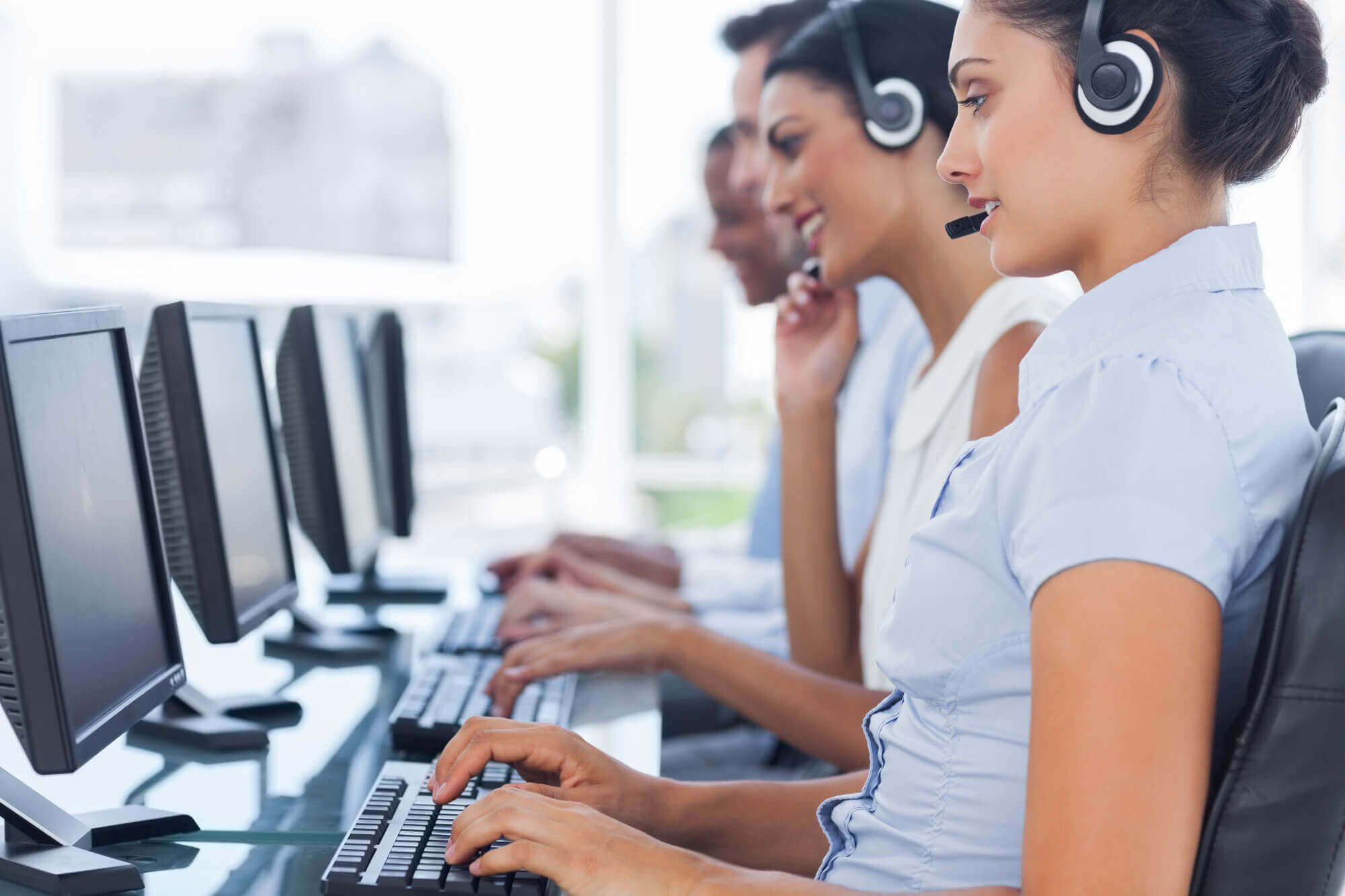 Side view of call center employees wearing VoIP headsets and using computers