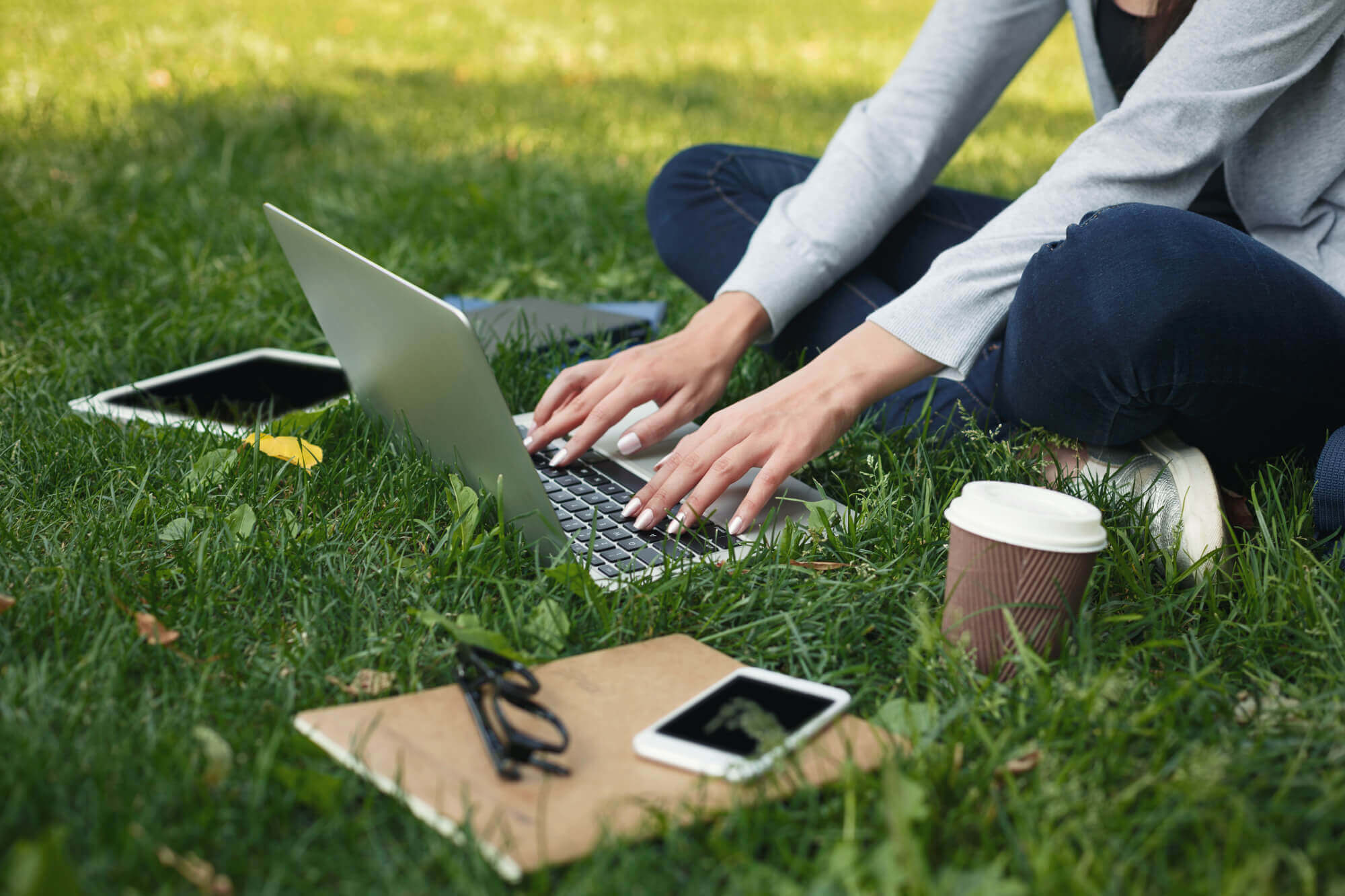 Woman sitting on grass using a silver laptop