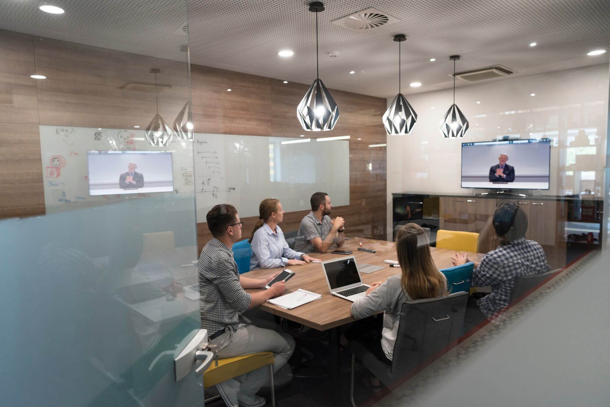 Group of workers sitting at conference table video conferencing with an older businessman