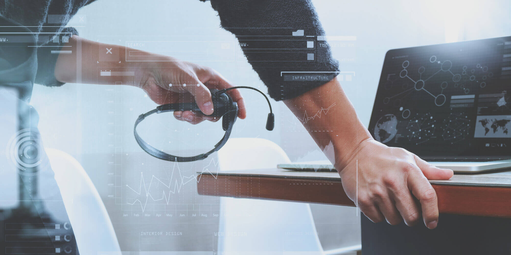 Man's arms holding a VoIP headset and leaning on a desk in front of a laptop